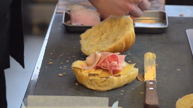 Ham being placed on a croissant