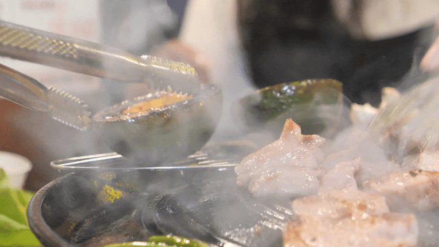 Tongs grilling meat and avocado on a hot iron plate