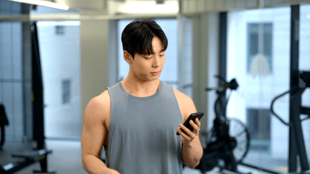 Young man focused on smartphone while using dumbbells at gym