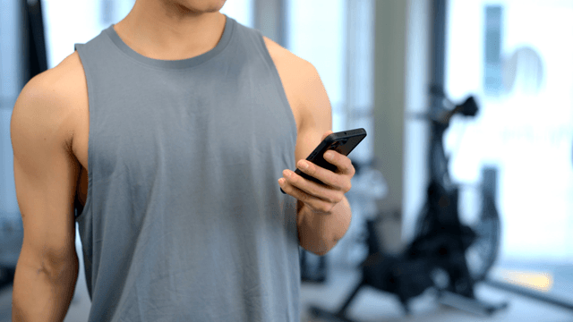 Man using smartphone while lifting a small dumbbell at gym
