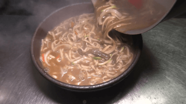 Noodle soup being transferred into a ceramic bowl