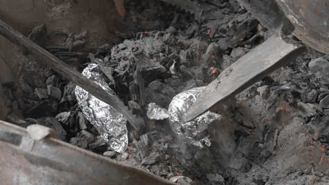 Foil-wrapped sweet potatoes roasting on hot charcoal fire