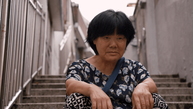 An elderly woman sitting on outdoor stairs