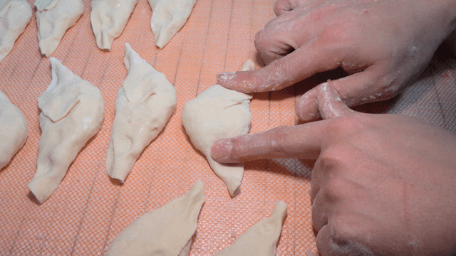 쟁반 위에 만두를 눌러 모양을 잡는 손