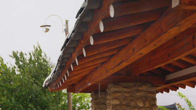 Traditional Korean gate eaves in rain with wooden pillars