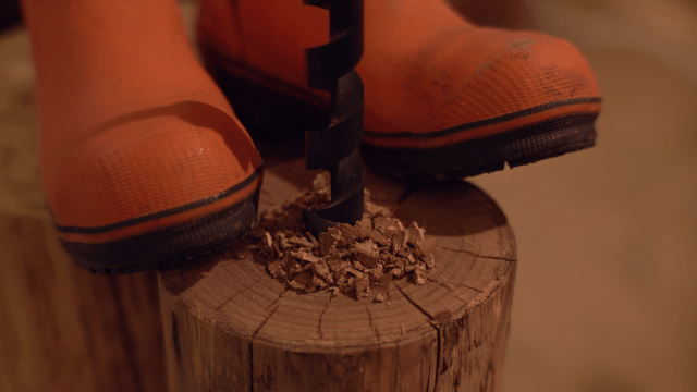 Drilling into a wooden log with orange boots