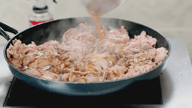 Pouring sauce over sizzling meat in a pan