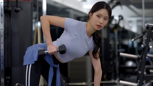 Young woman doing dumbbell row on gym bench