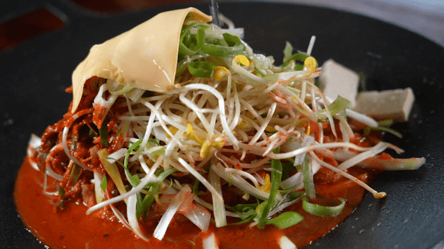 Broth poured over budaejjigae topped with cheese and bean sprouts