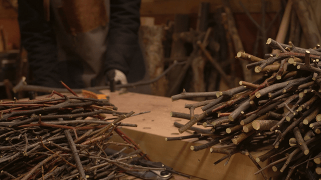 Craftsman trimming a pile of wooden branches in workshop