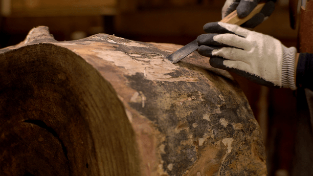 Artisan carving the surface of a wooden barrel with a chisel