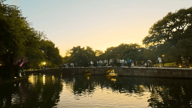 People walking on a stone bridge over an evening pond