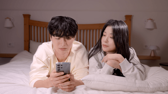 Couple talking in bed while looking at smartphone
