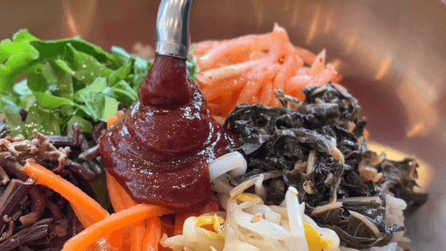 Spicy red pepper paste being poured over bibimbap
