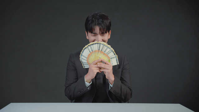 Man smiling with his mouth covered by money