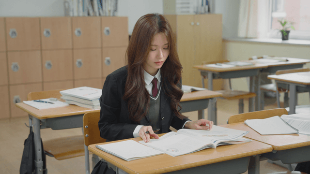 Student taking notes in a notebook while studying with a textbook in the classroom