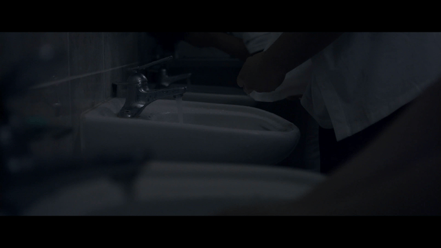Person washing hands and shirt in dark bathroom