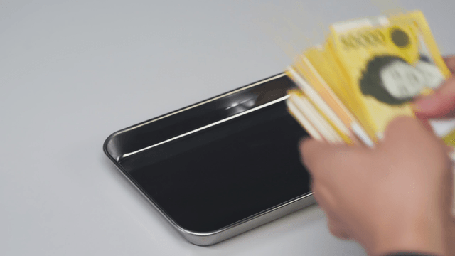 A hand picking up a Korean won from a tray