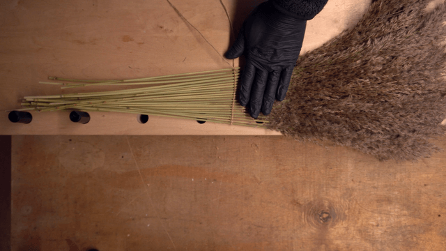 Hands crafting with dried reeds on a table