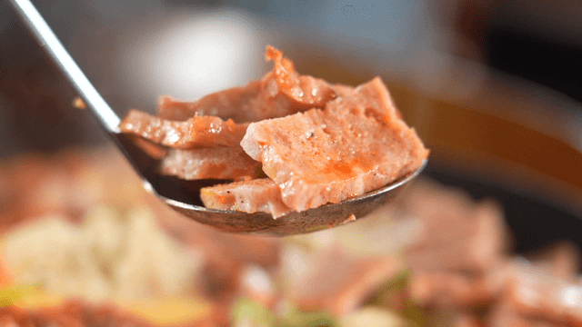 Ladle scooping sizzling stir-fried sausage from hot pan