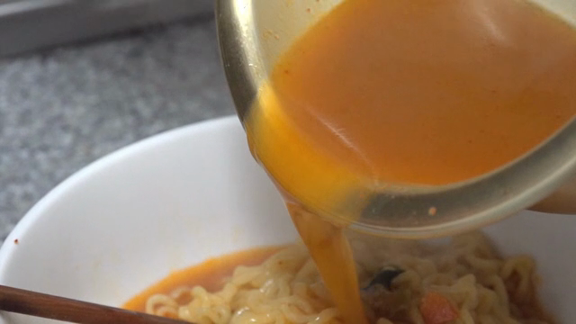 Pouring broth into a bowl of ramyeon