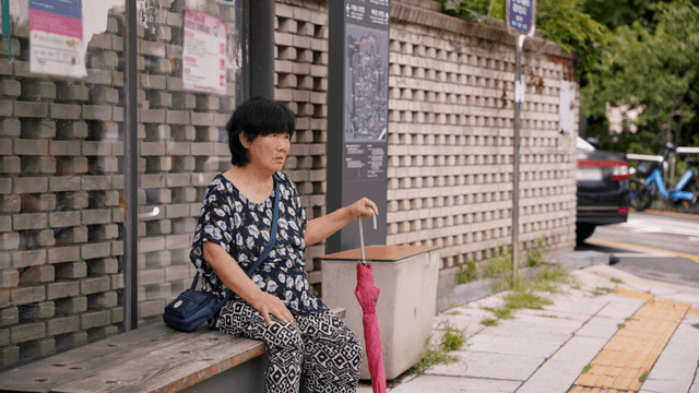 An elderly woman sitting at a bus stop talking