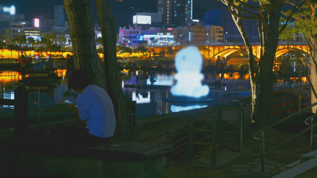 Night lights illuminating sculpture by riverbank bench with person