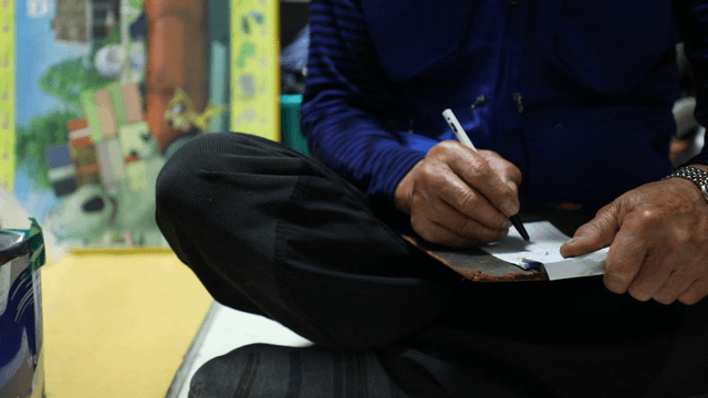 Elderly person writing indoors on a bill