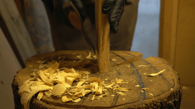 Artisan shaping a wooden piece with an axe on a wood block