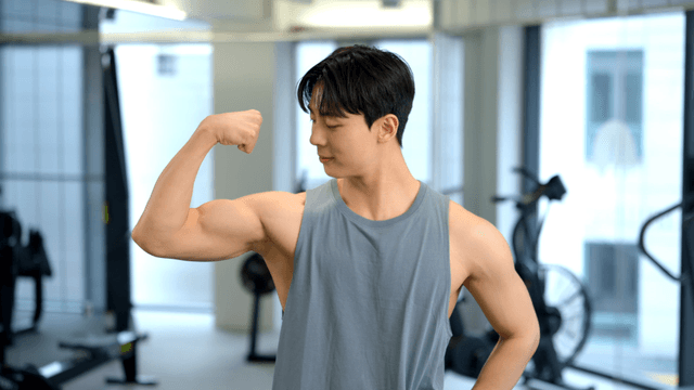 Young man flexing arm muscles at gym
