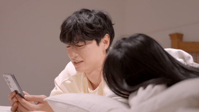 Couple relaxing on bed while looking at smartphone