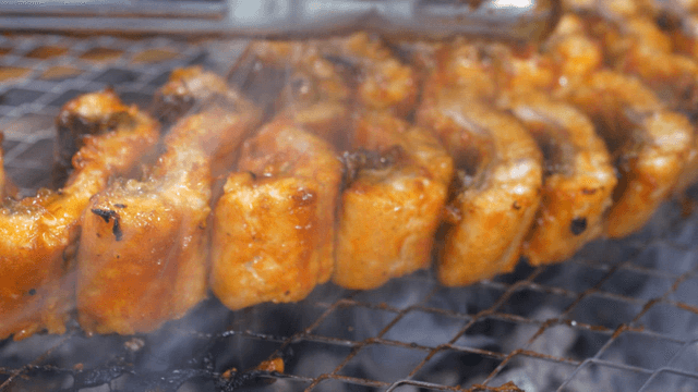 Tongs flipping spicy seasoned eels on grill