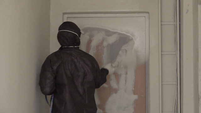 Worker spraying paint on a door in a narrow hallway