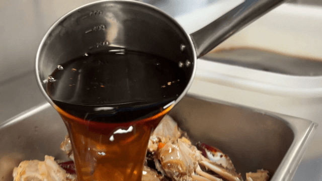 Ladle pouring special soy sauce over marinated crab