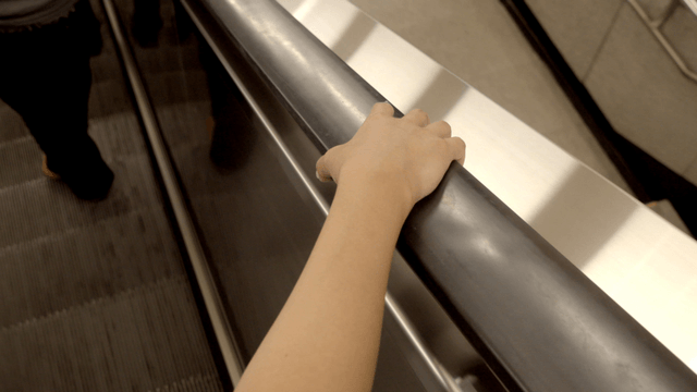 Hand holding an escalator railing indoors