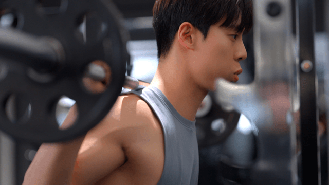 Young man performing squat with weighted bar on shoulders