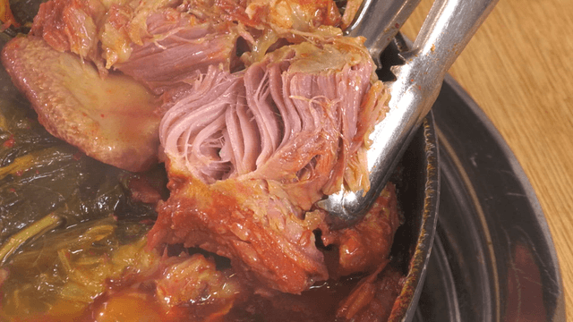 Tongs tearing tender pork back-bone meat from outer leaves stew