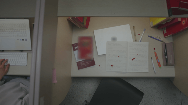 Empty desk with a nosebleed beyond the students studying at the reading room desks.