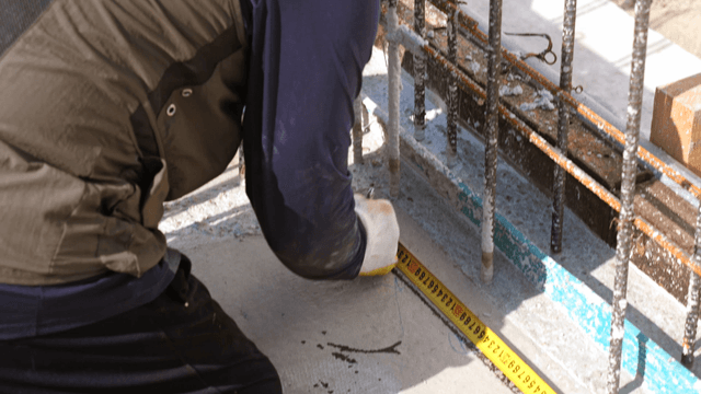 Worker measuring concrete with tape measure