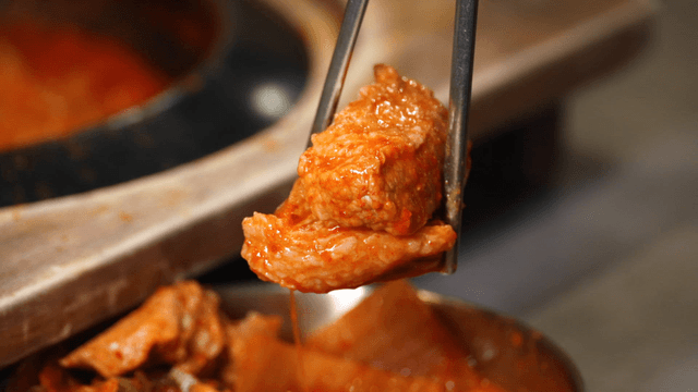 Large pork piece lifted from kimchi stew with chopsticks