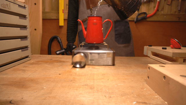 Worker boiling water with a red kettle on a portable burner