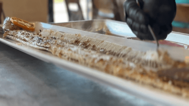 Hands preparing grilled cutlassfish fillets with knife and spoon