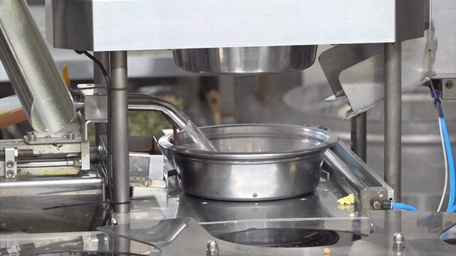 A machine filling a metal bowl with liquid