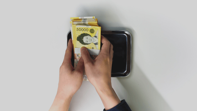 A hand picking up a Korean won from a tray