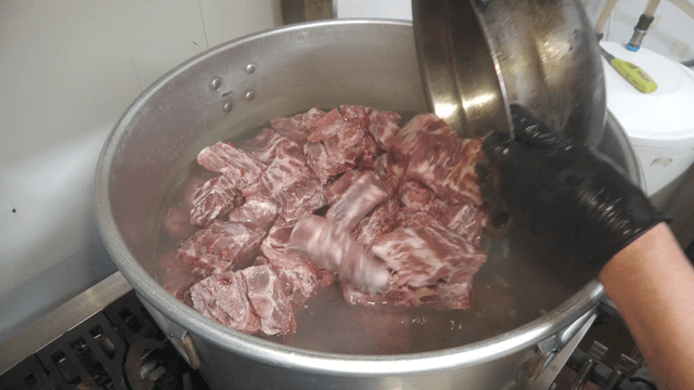 Meat being placed into a large pot filled with water
