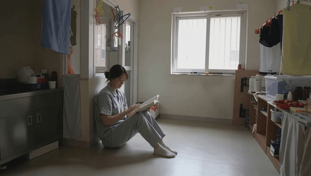 Female inmate reading alone in prison cell