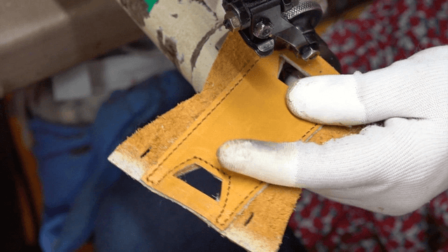 Worker sewing leather with sewing machine