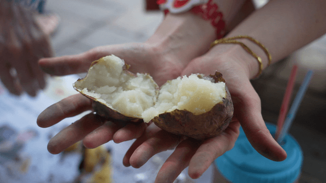 Hands splitting the skin of roasted potato in half