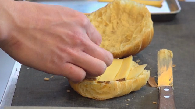 Cheese being placed on a croissant