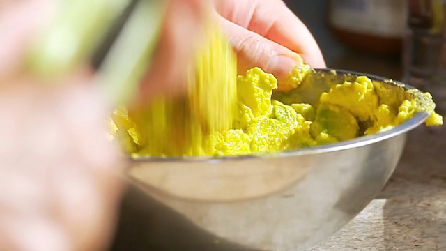Hands mashing avocado in a metal bowl